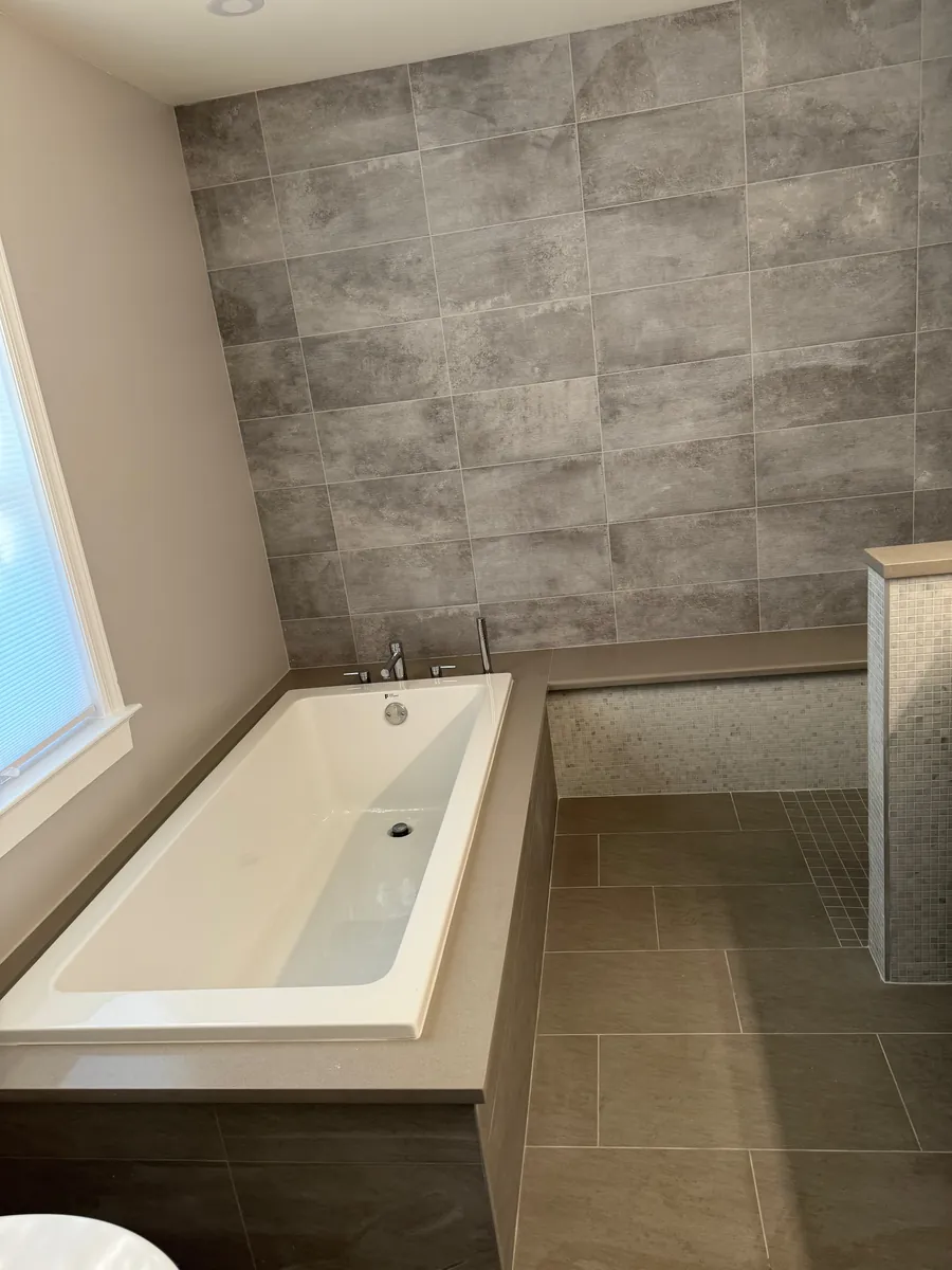 Remodeled bathroom with an alcove soaking tub, large-format gray wall tile and a bright window in Stamford, CT