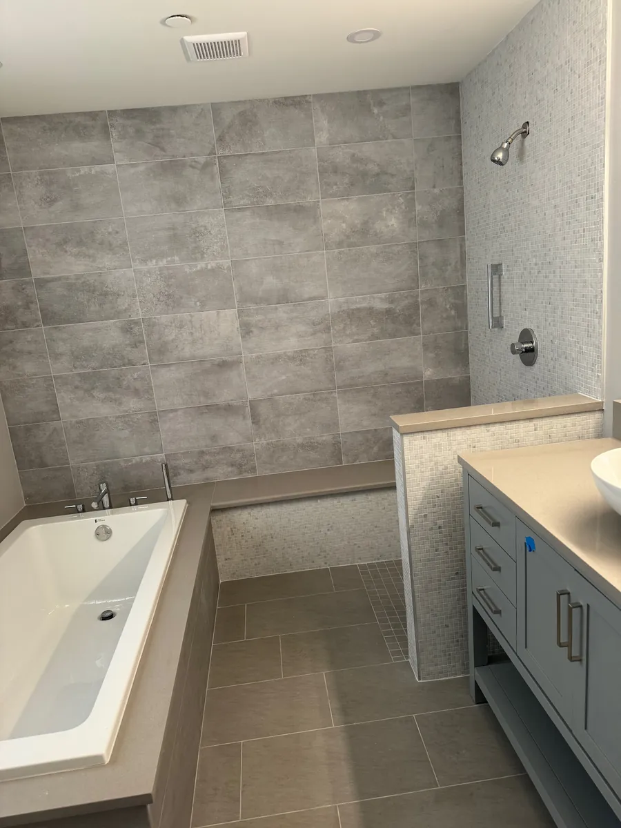 Bathroom with a gray tile tub surround, wall-mounted shower fixture and a gray vanity with a vessel sink in Stamford, CT