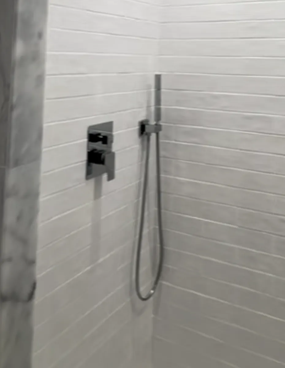 Tiled shower wall with a new mixing valve and handheld shower on a slide bar