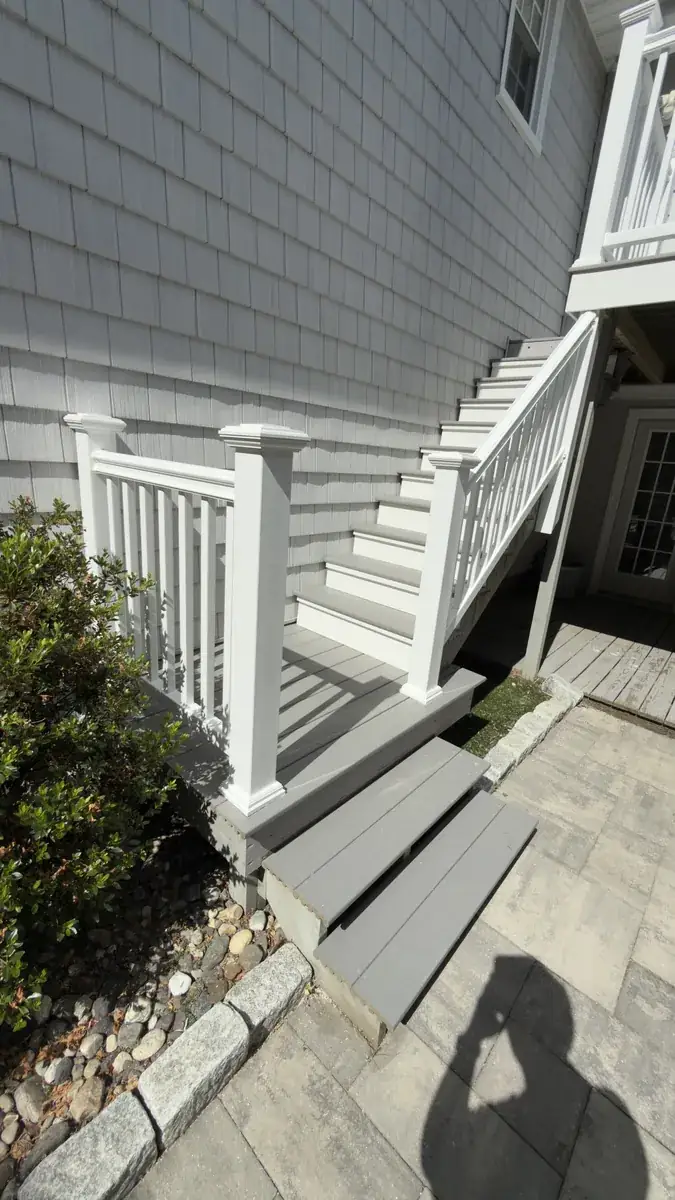 Deck stairs and white railing built along the side of a shingled house in Stratford, CT