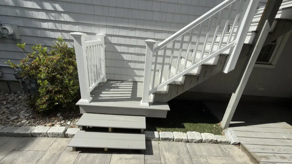 New deck stairs with white railing leading down to a paver patio