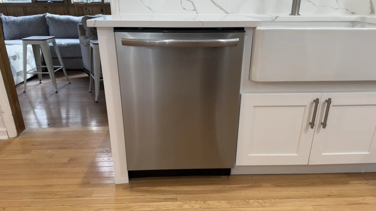 Stainless dishwasher and farmhouse sink under a quartz countertop with hardwood flooring in Stratford, CT