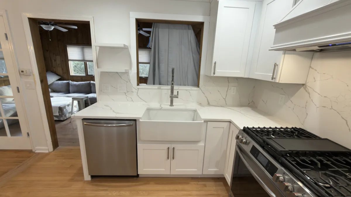 Kitchen sink wall with a farmhouse sink, pull-down faucet and full-height quartz backsplash beside a window opening in Stratford, CT