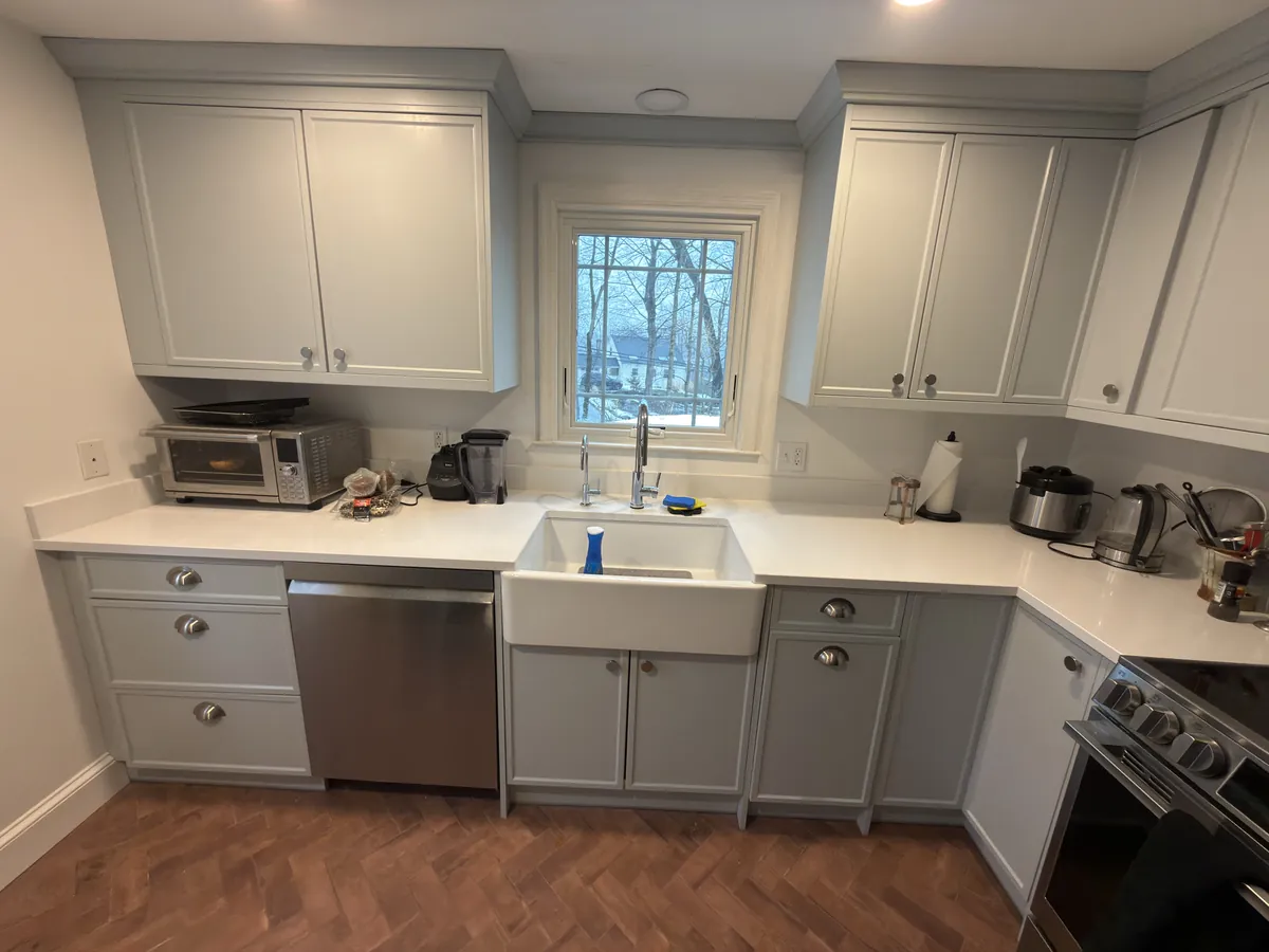 Light gray shaker cabinets with a farmhouse sink under the window and a herringbone wood floor in Westport, CT