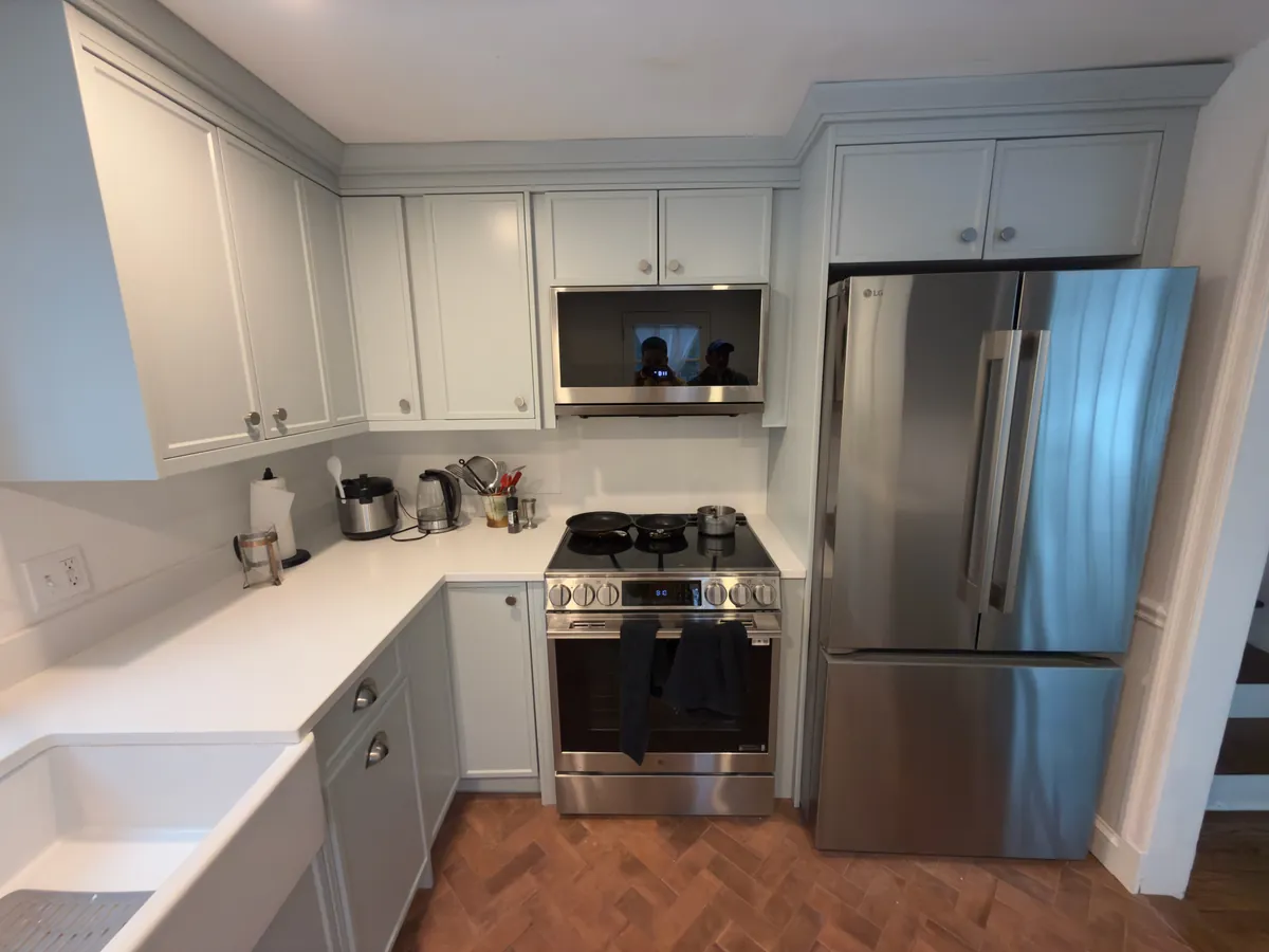 Remodeled kitchen with light gray shaker cabinets, stainless refrigerator and range, white quartz counters and herringbone wood floor in Westport, CT