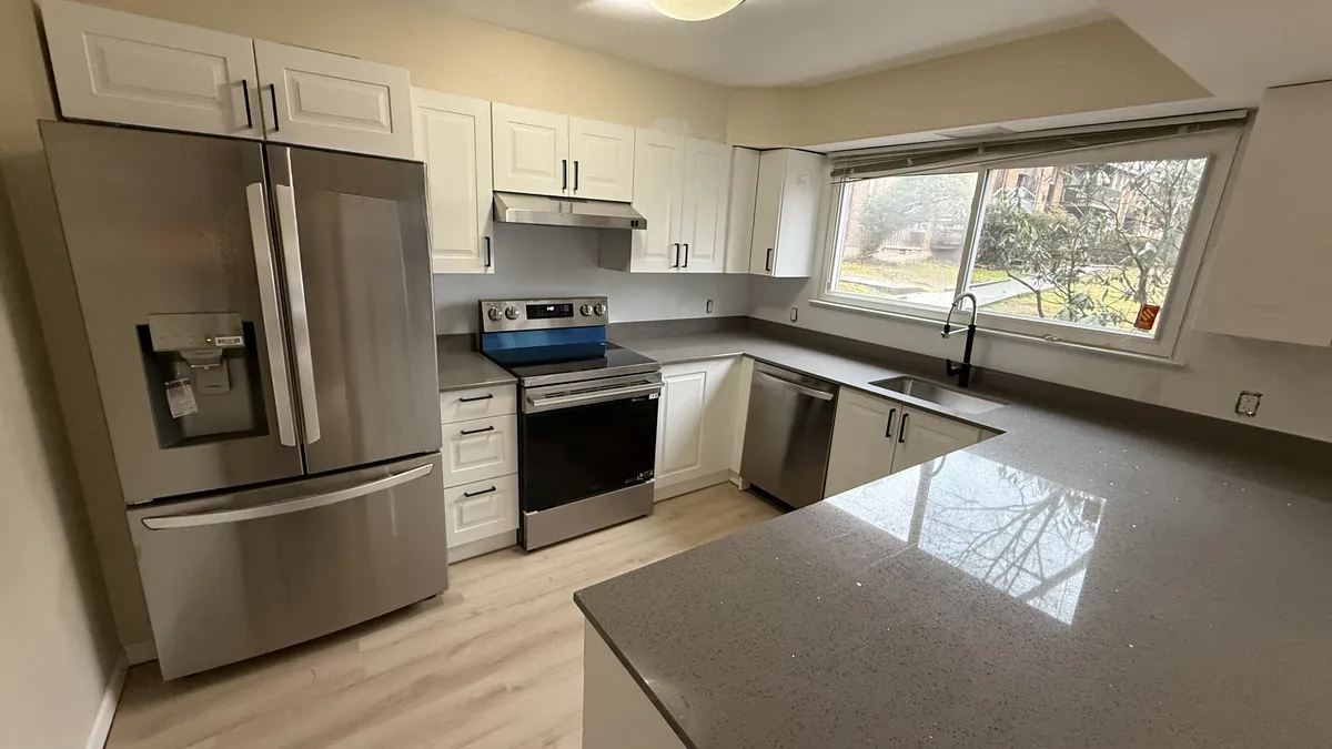 L-shaped kitchen with white cabinets, a gray quartz peninsula, stainless appliances and wood-look flooring in Bridgeport, CT