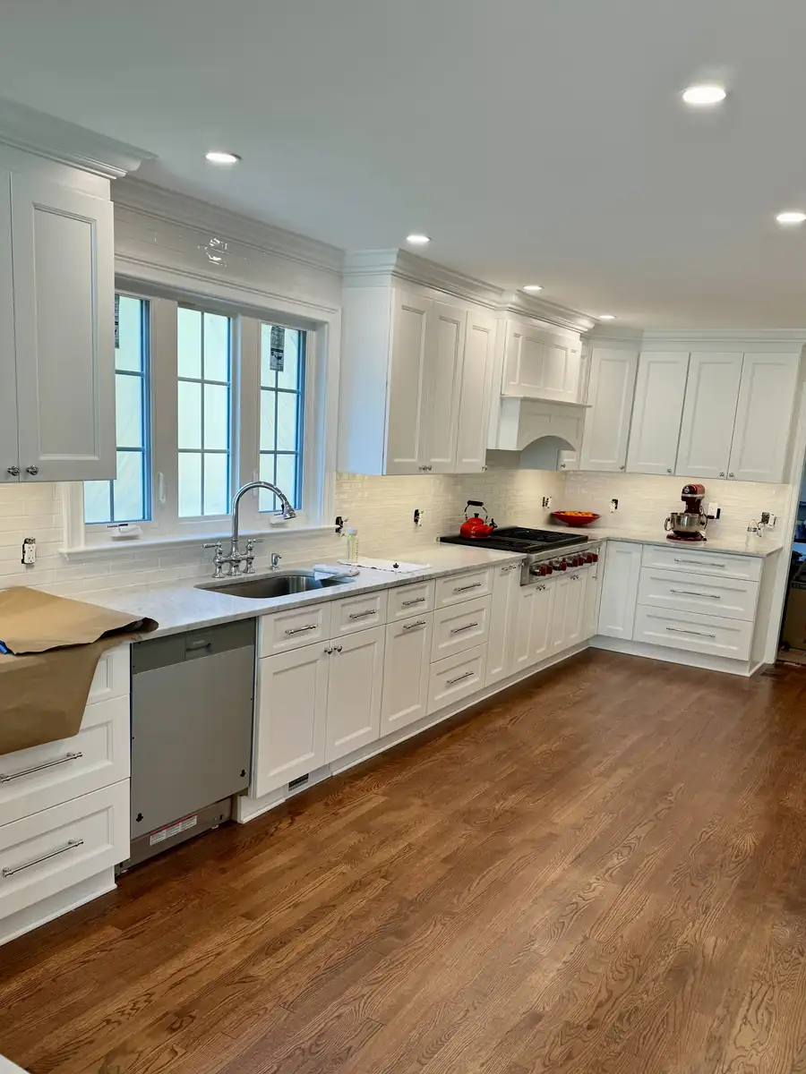 Long run of white cabinets with quartz counters, a stainless dishwasher and hardwood floors under a bank of windows in Weston, CT