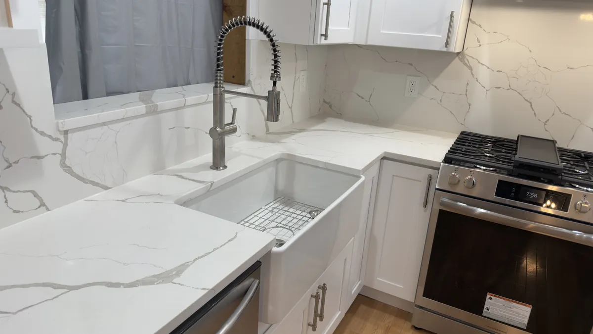 Close-up of a marble-look quartz backsplash, farmhouse sink and commercial-style faucet next to a gas range in Stratford, CT