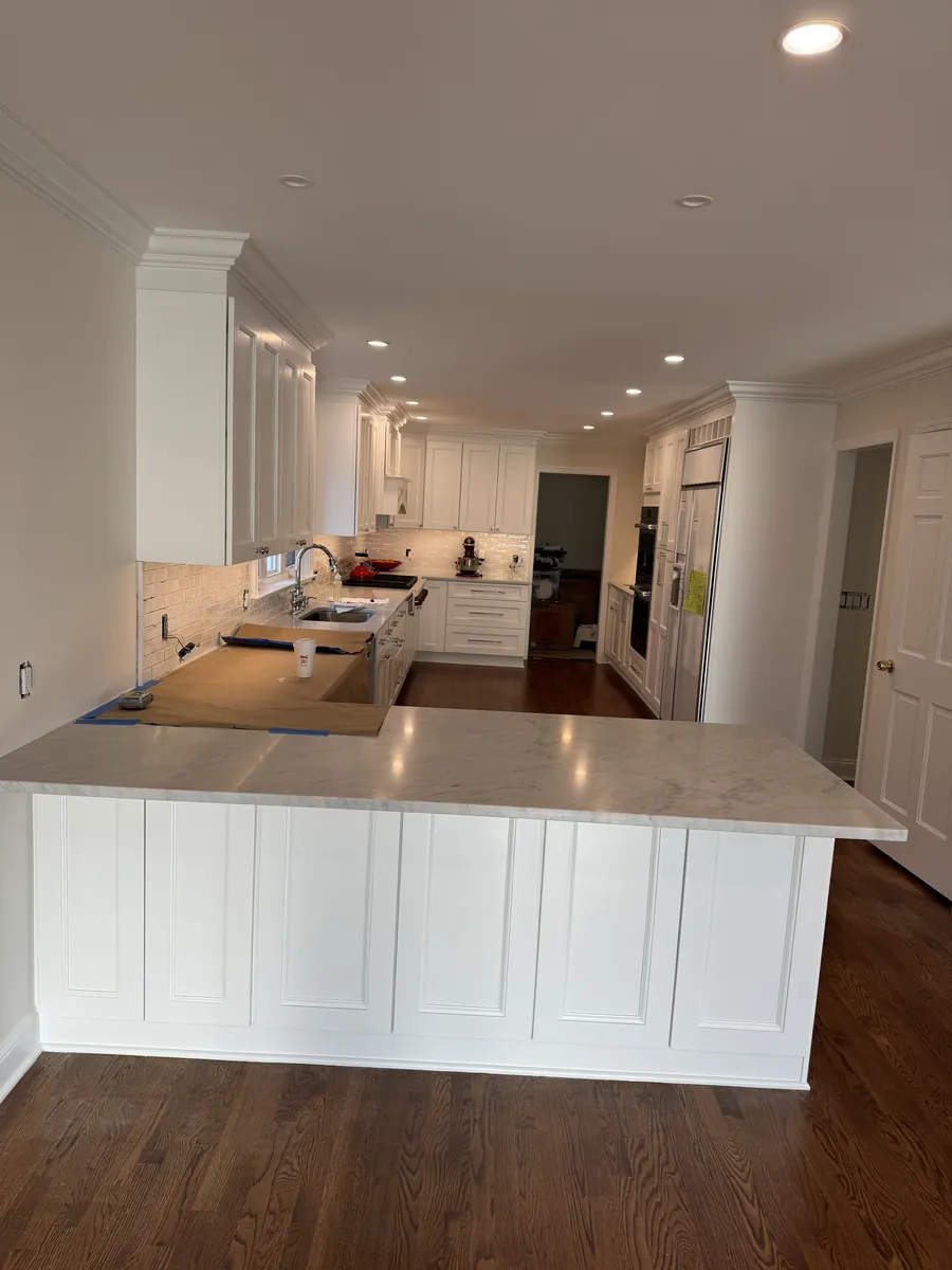 White shaker kitchen with a quartz peninsula, crown molding and recessed lighting in Weston, CT