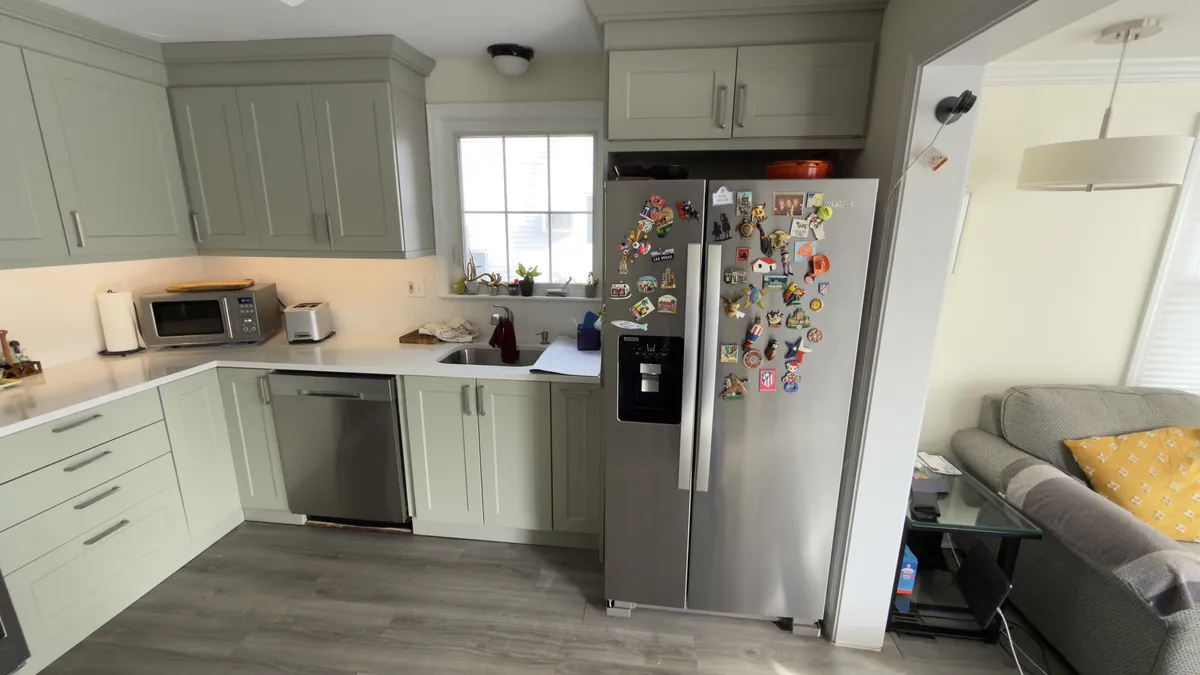Sage green shaker kitchen open to the living room, with a stainless refrigerator and gray plank floor in Fairfield, CT