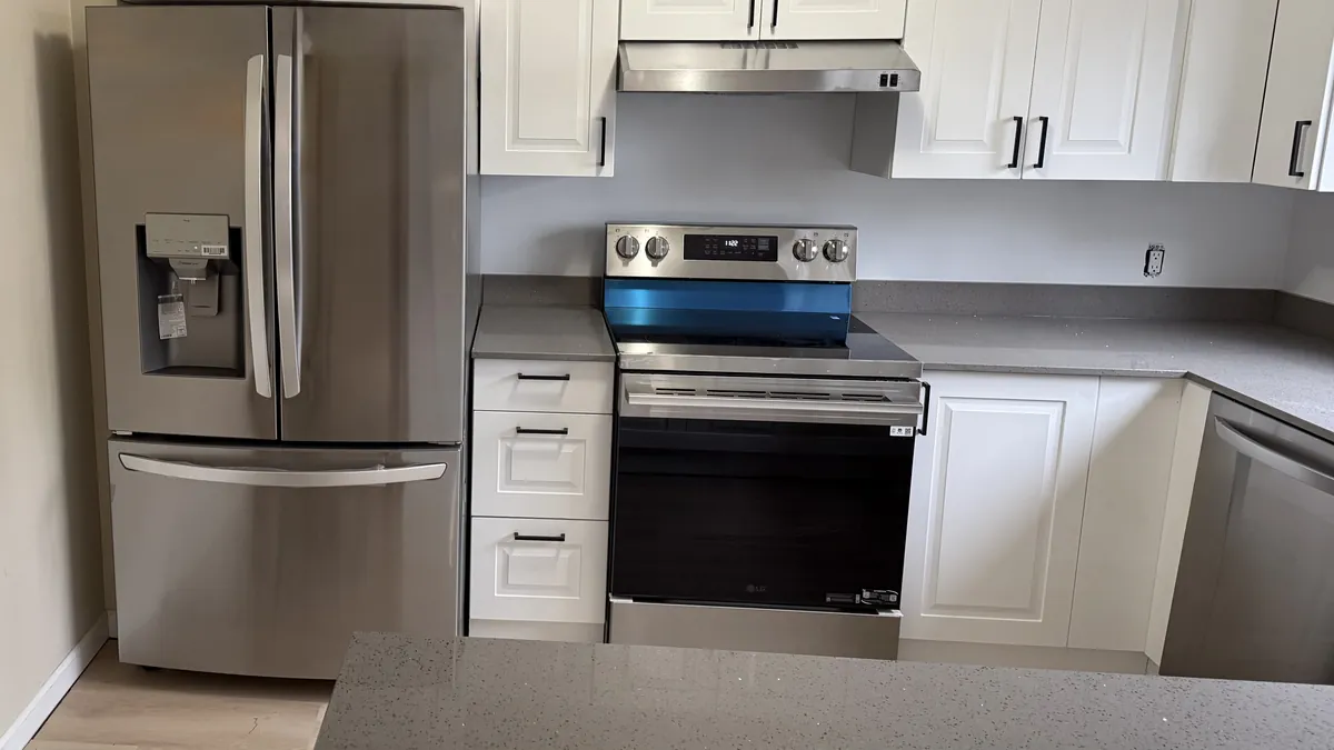Stainless refrigerator and electric range between white cabinets with gray quartz counters in Bridgeport, CT