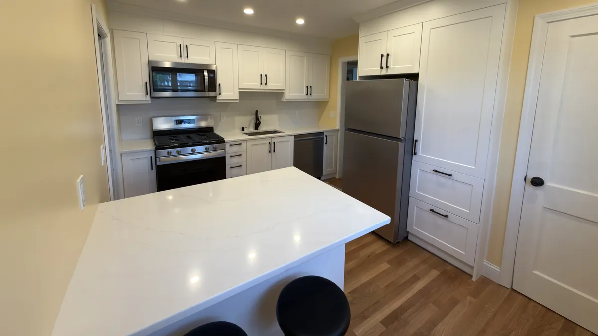 White shaker kitchen with a quartz island, gas range, over-range microwave and tall pantry cabinet in Stratford, CT
