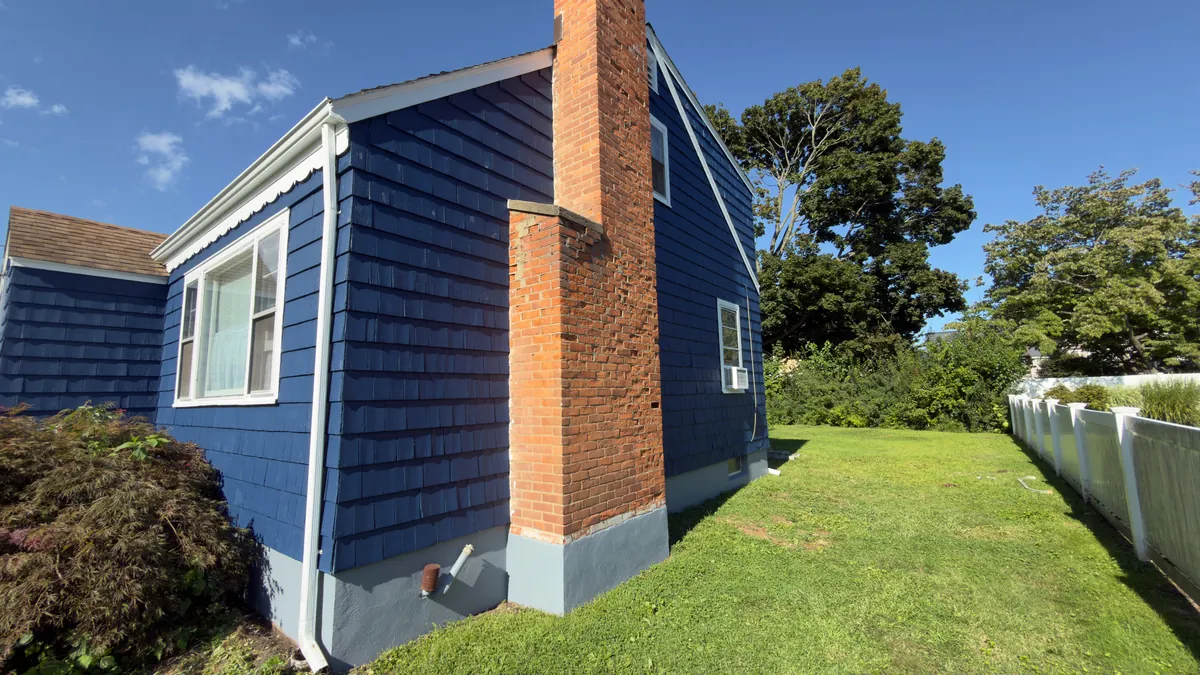 Rear corner of a navy blue house with white trim, a brick chimney and a freshly painted gray foundation in Stratford, CT