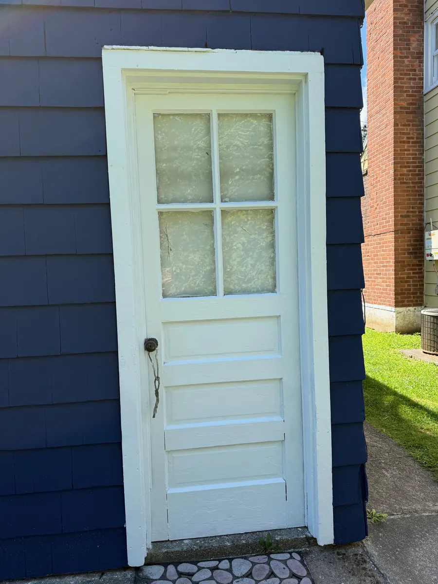 Side entry door and frame painted white against navy blue shingle siding in Stratford, CT